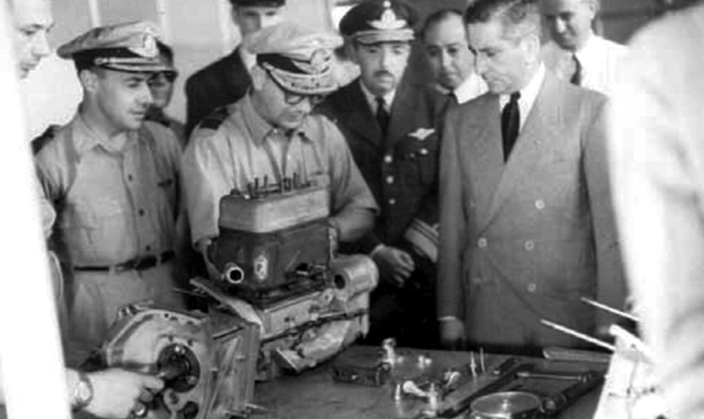 El Ministro de Aeronáutica Juan Ignacio San Martín y a su derecha el Administrador General de IAME Brigadier Mayor Alberto Nicolás Ferro Sessarego, observan el ensamblaje del primer motor de automóvil construido;detrás del Señor Ministro se encuentra Ambrosio Taravella. 1952.